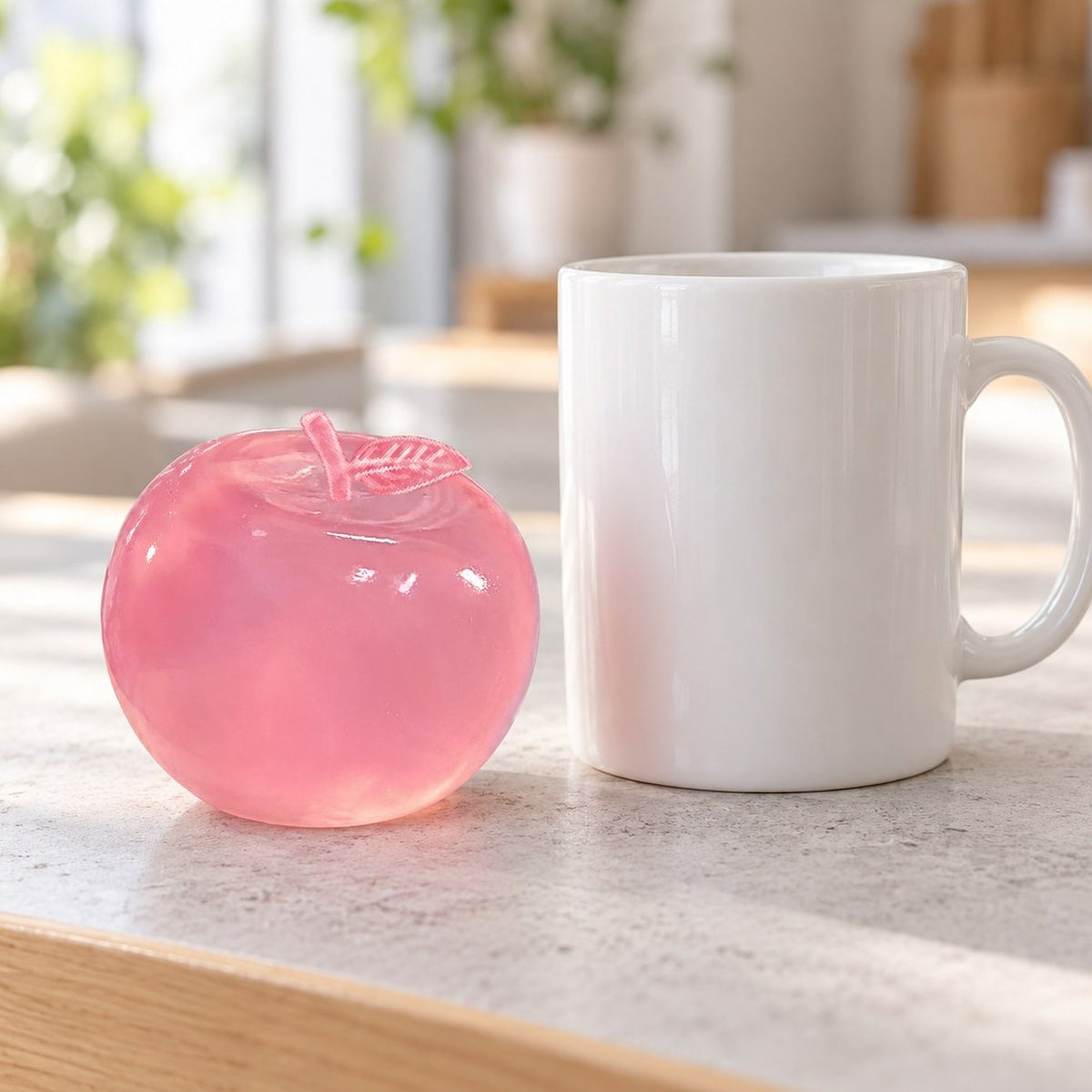 Poederroze rekbare appel squishy naast een koffiemok om de grootte te vergelijken
