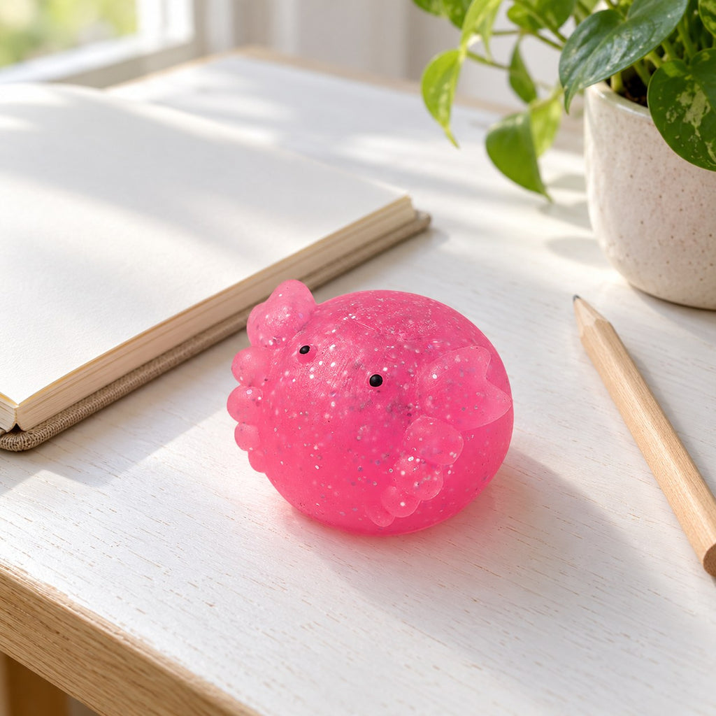 Axolotl squishy mochi glitter, on a desk with a notebook and pencil