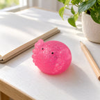 Axolotl squishy mochi glitter, on a desk with a notebook and pencil