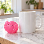 Axolotl Mochi Squishy with Glitter, next to a coffee mug for size comparison