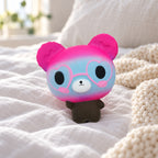 Bear Squishy with Heart Glasses, Slow Rising, 12 cm (Pink and blue), on a cozy bed with soft blankets