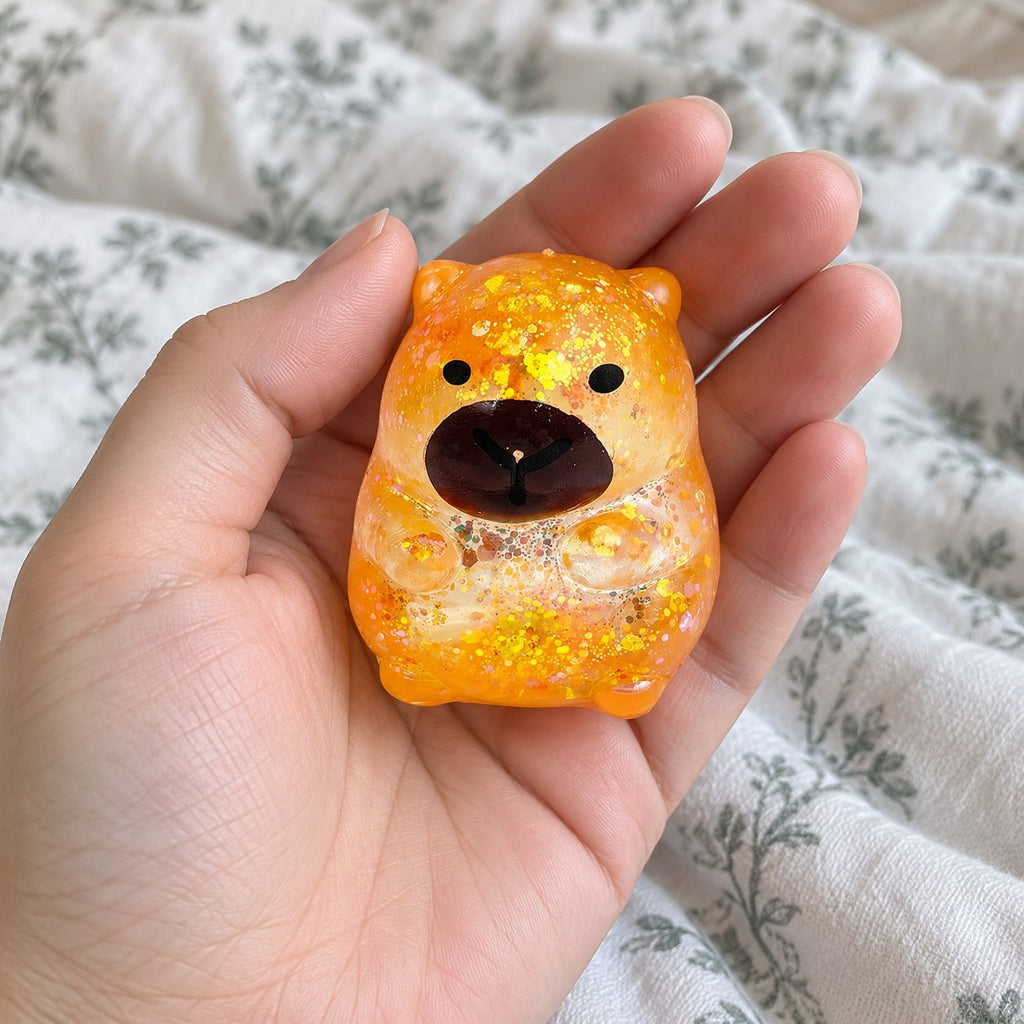 Capybara squishy glitter (orange), held toward the camera, first-person view