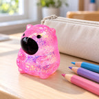 Capybara squishy with glitter (pink), on a school desk next to a pencil case
