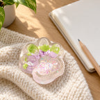 Cat paw squishy glitter (Lilac), on a desk with a notebook and pencil