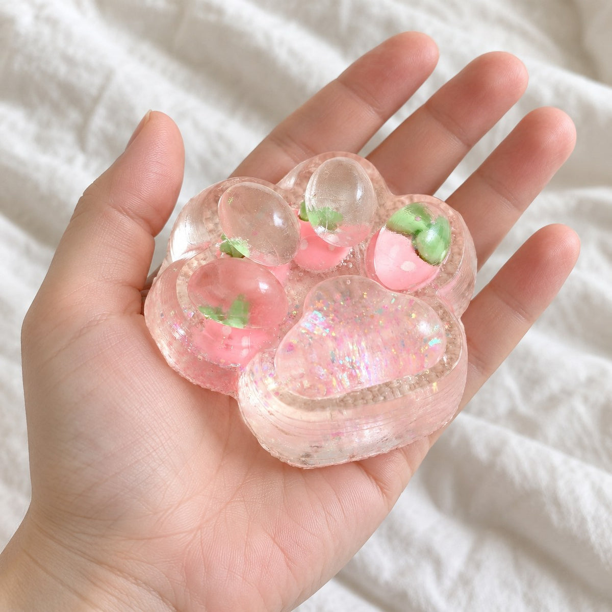 Cat paw squishy glitter jelly (Strawberry pink), held toward the camera, first-person view