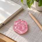 Mini Jelly Cat Paw Squishy, 4 cm (Pink glitter), on a desk with a notebook and pencil