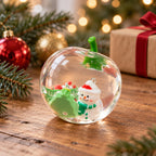 Squishy manzana navideña, transparente con muñeco de nieve, en una escena navideña con ramas de abeto y luces