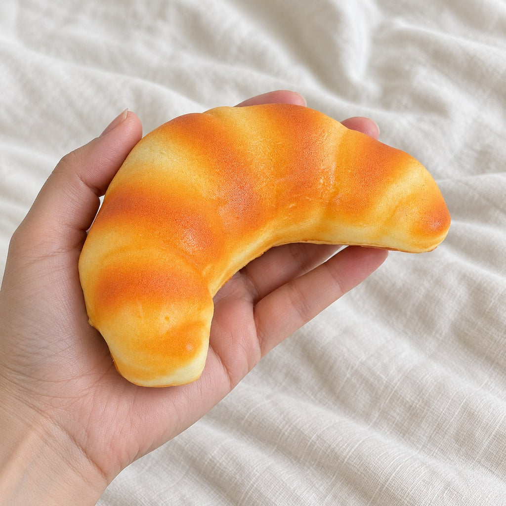 Croissant squishy (12.5 cm), held toward the camera, first-person view