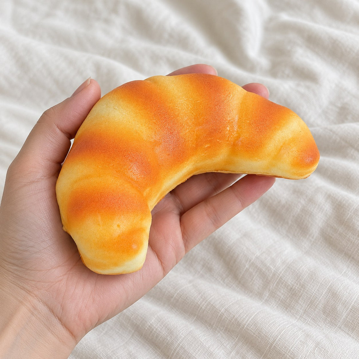 Croissant squishy (12.5 cm), held toward the camera, first-person view