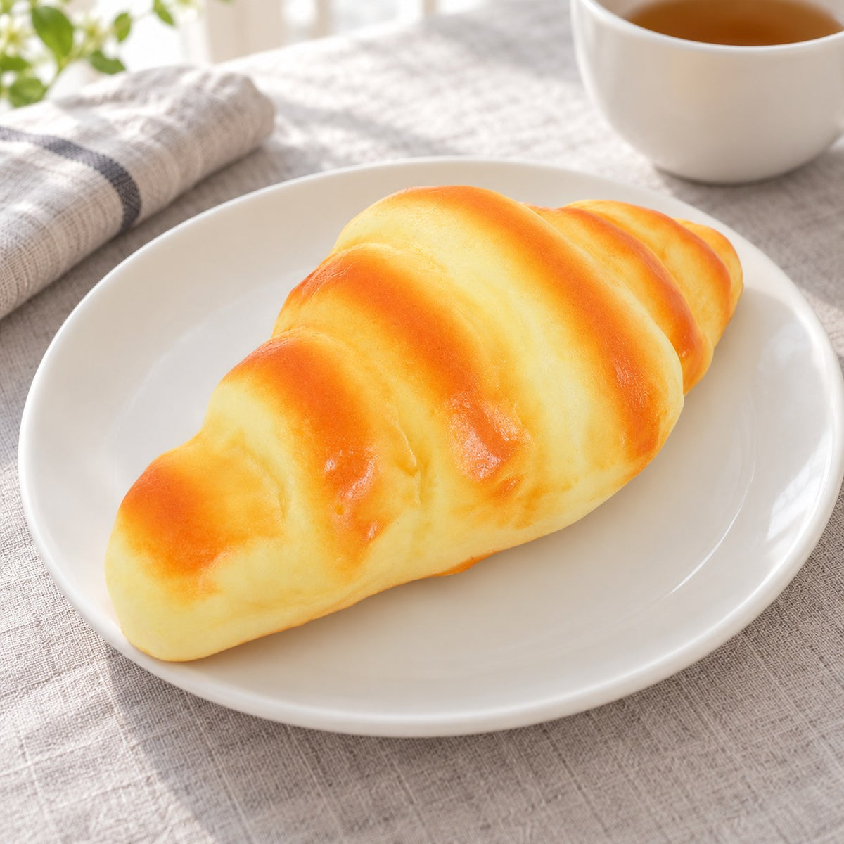 Croissant Squishy, Realistic Slow Rising Bread (16 cm), on a plate on a breakfast table