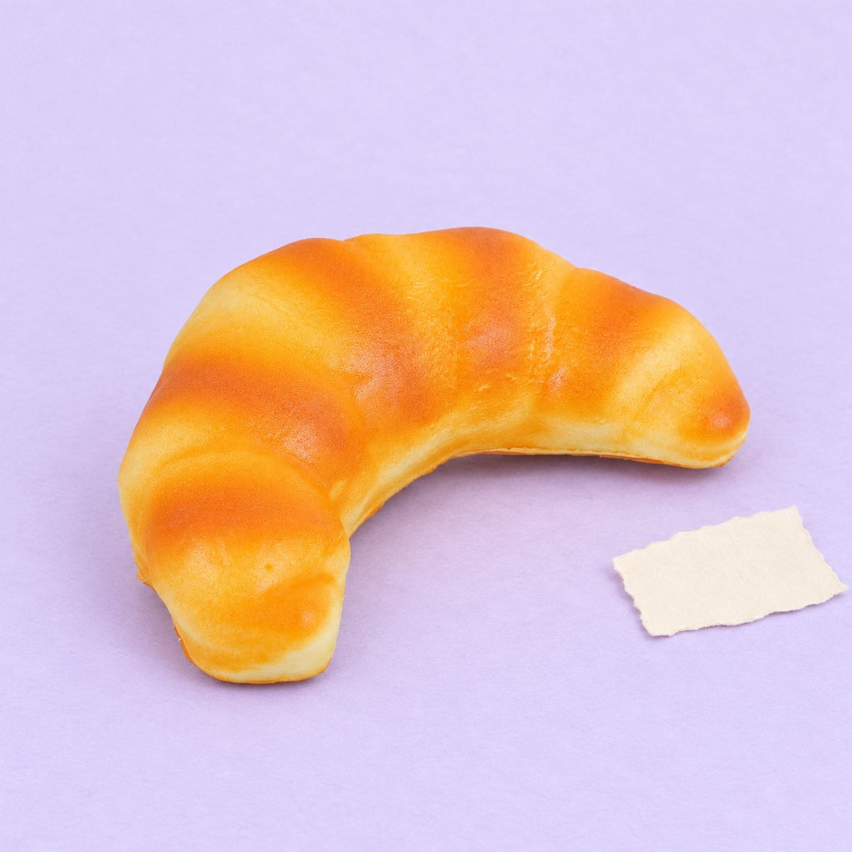 Croissant squishy slow rising van 12,5 cm, realistisch brood, op pastelkleurig papier