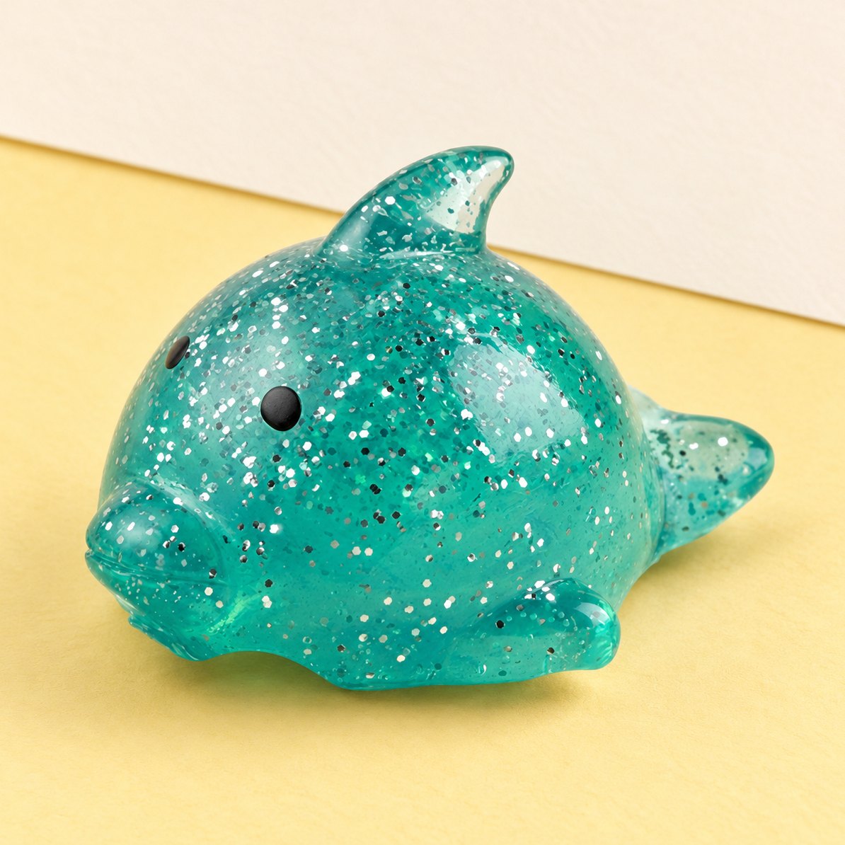 Stor delfin-squishy med glimmer, produktfoto på pastelfarvet papir