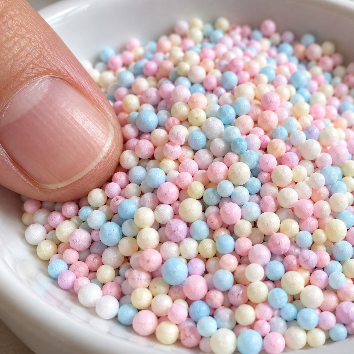 Pastel foam beads for paper squishies, close up with a fingertip for size