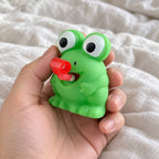 Squishy groda eller dino som räcker ut tungan (Groda, slumpvis färg), hålls mot kameran ur eget perspektiv