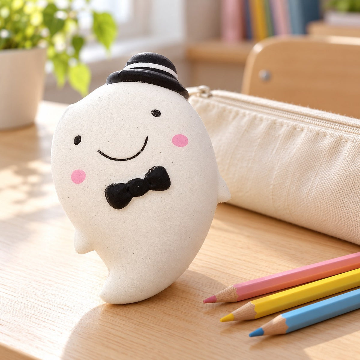 Slow Rising Ghost Squishy, 14.5 cm (white), on a school desk next to a pencil case