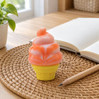 Ice Cream Cone Squishy, Stretchy Silicone (orange), on a desk with a notebook and pencil