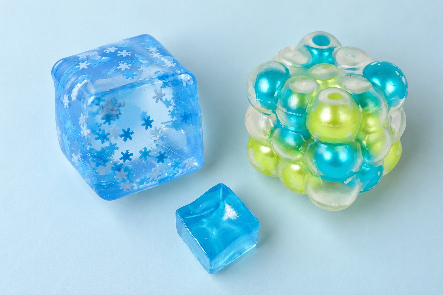 Three clear ice cube squishies seen from above on ice blue: mini cube, snowflake cube and bubble cube with pearls