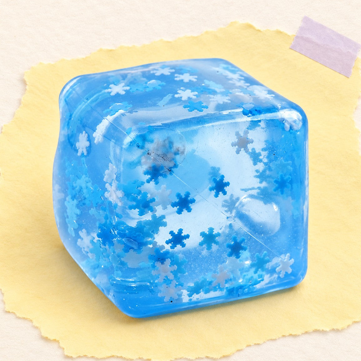 Squishy kostka lodu – Squishy kostka lodu 5 cm, śnieżynka, marmurek lub brokat (Śnieżynka, w woreczku), zdjęcie produktu na pastelowym papierze