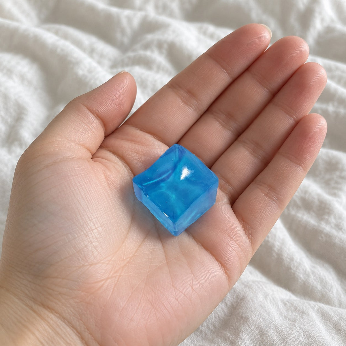 Ice cube squishy mini jelly (blue), held toward the camera, first-person view
