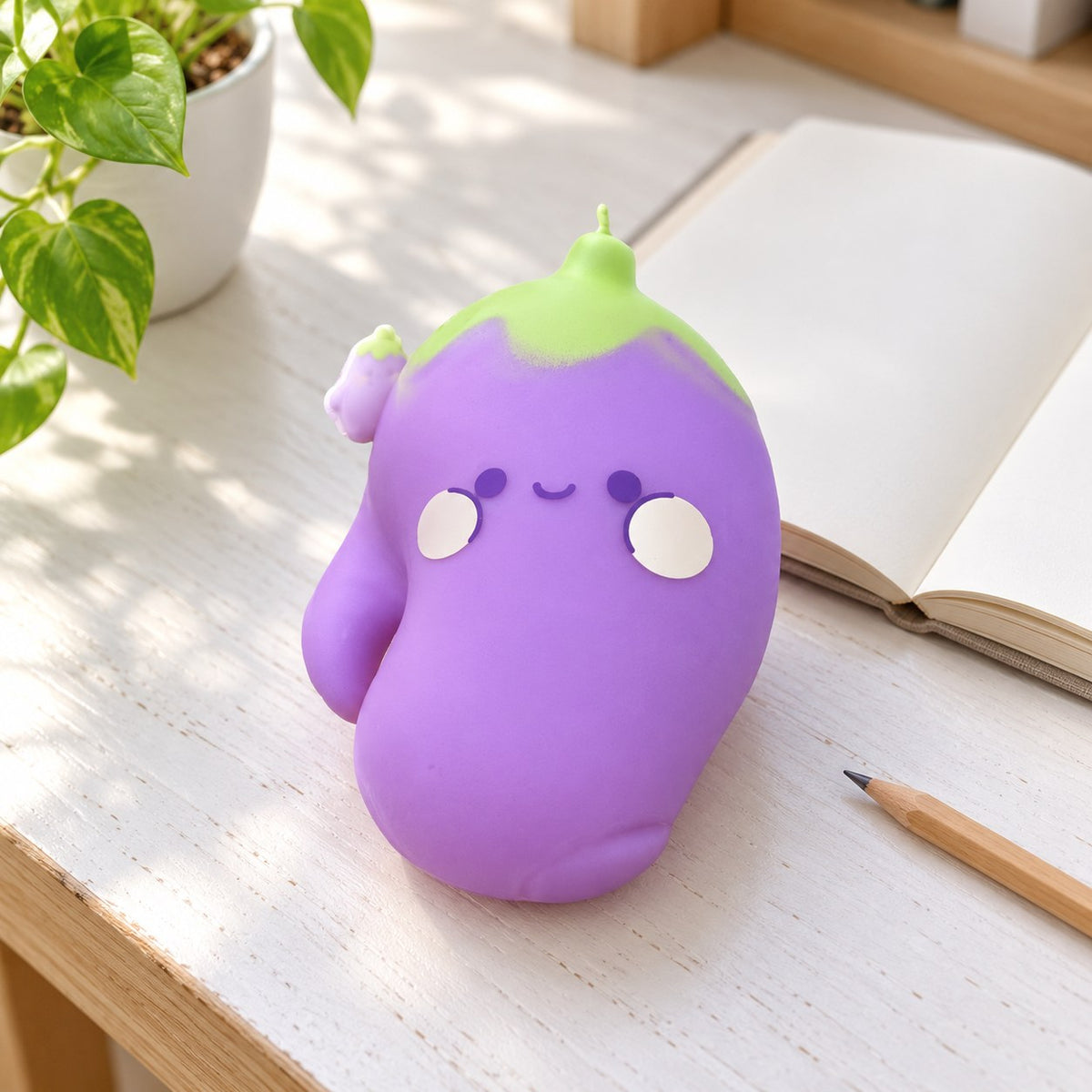 Squishy melanzana jumbo, faccina kawaii, su una scrivania con quaderno e matita