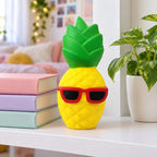 Jumbo Pineapple Squishy with Sunglasses, on a shelf with books and a plant as room decor