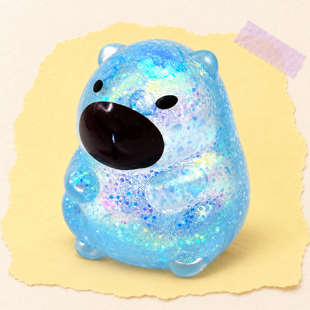 Blå kapybara-squishy med glimmer i sugar-stil, produktfoto på pastelfarvet papir