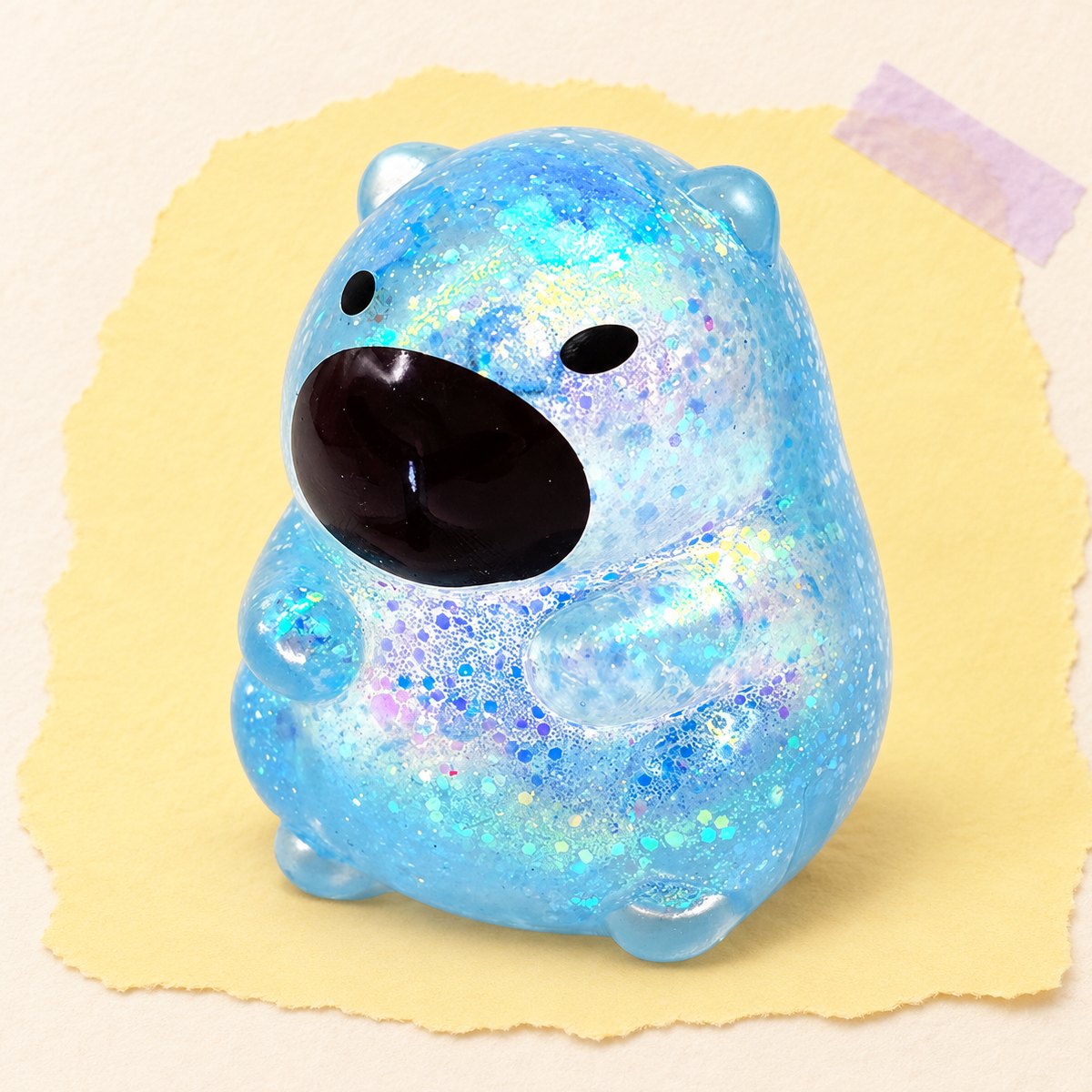Blå kapybara squishy med glitter och sockerfyllning på pastellpapper