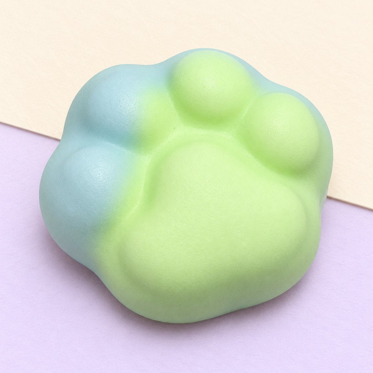 Grøn crunchy kattepote-squishy på 6 cm, produktfoto på pastelfarvet papir