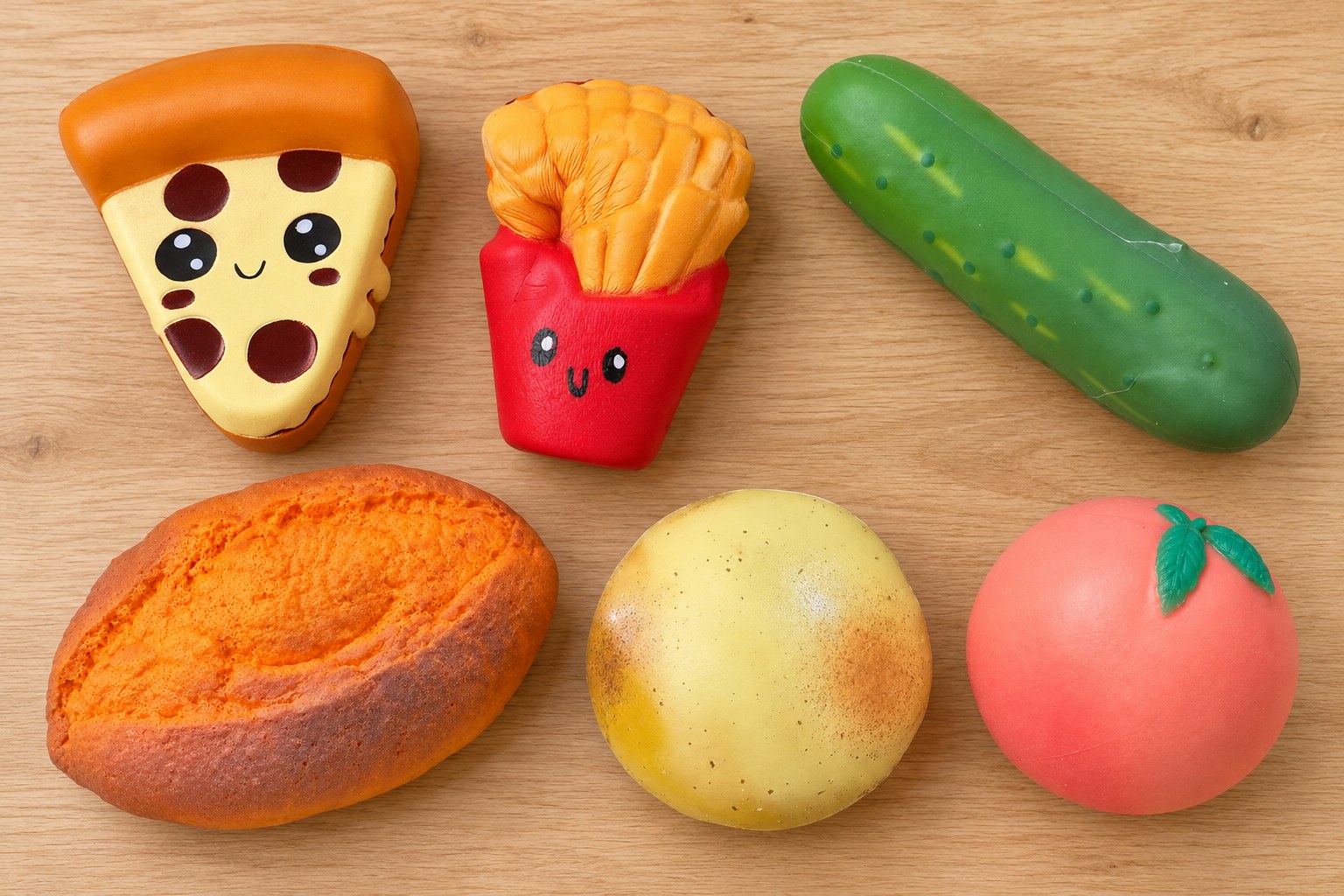 Mat-squishies ovanifrån på ett köksbord i trä: pizzabit, pommes frites, gurka, sötpotatis, potatis och persika