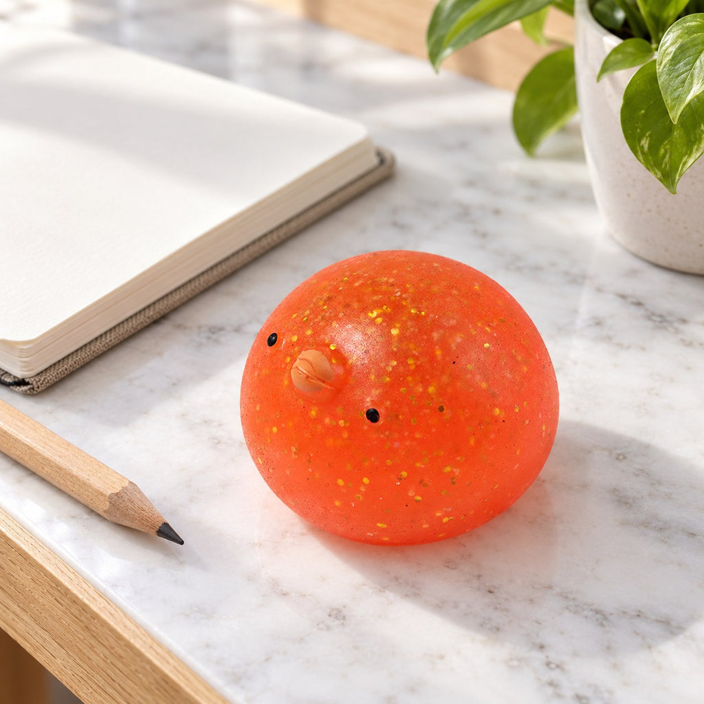 Mochi Squishy Chick with Glitter, on a desk with a notebook and pencil