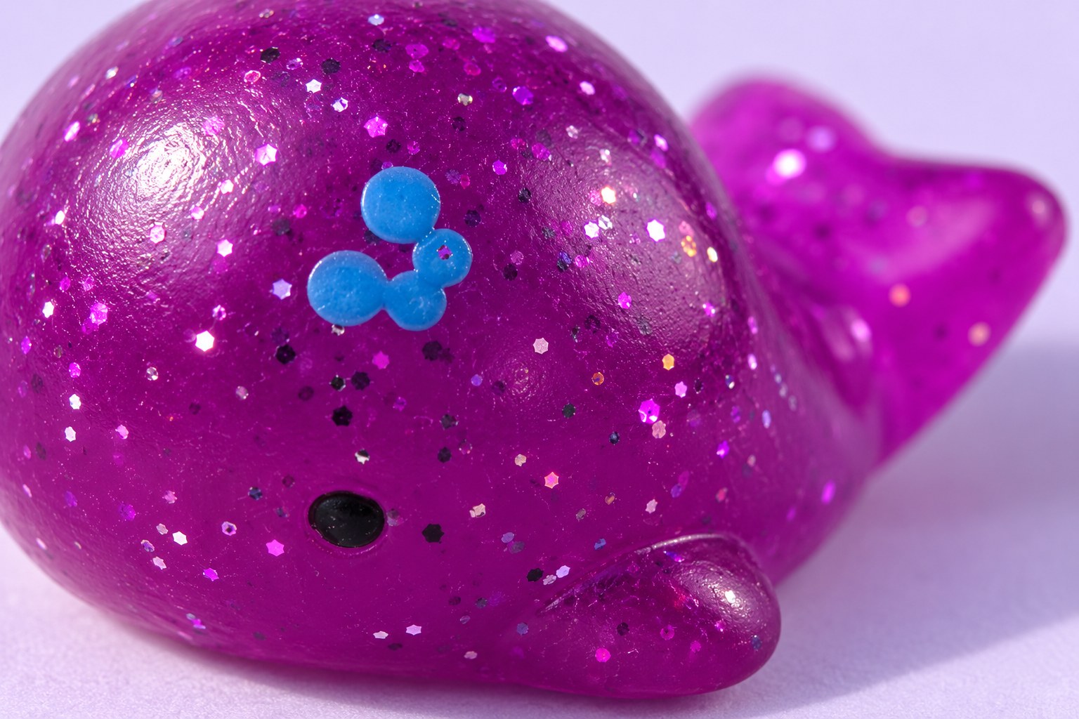 Close-up of a purple glitter mochi whale squishy, fine glitter sparkling inside the soft translucent skin