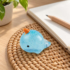 Mochi Squishy Narwhal with Glitter, on a desk with a notebook and pencil