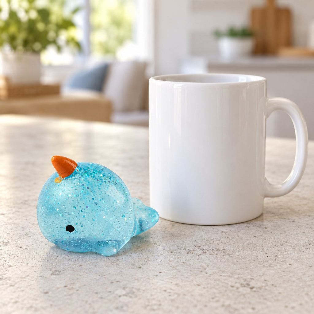Mochi Squishy Narwhal with Glitter, next to a coffee mug for size comparison