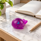 Mochi Squishy Whale with Glitter, on a desk with a notebook and pencil