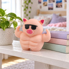 Muscle Pig Squishy with Sunglasses, 12.5 cm, on a shelf with books and a plant as room decor