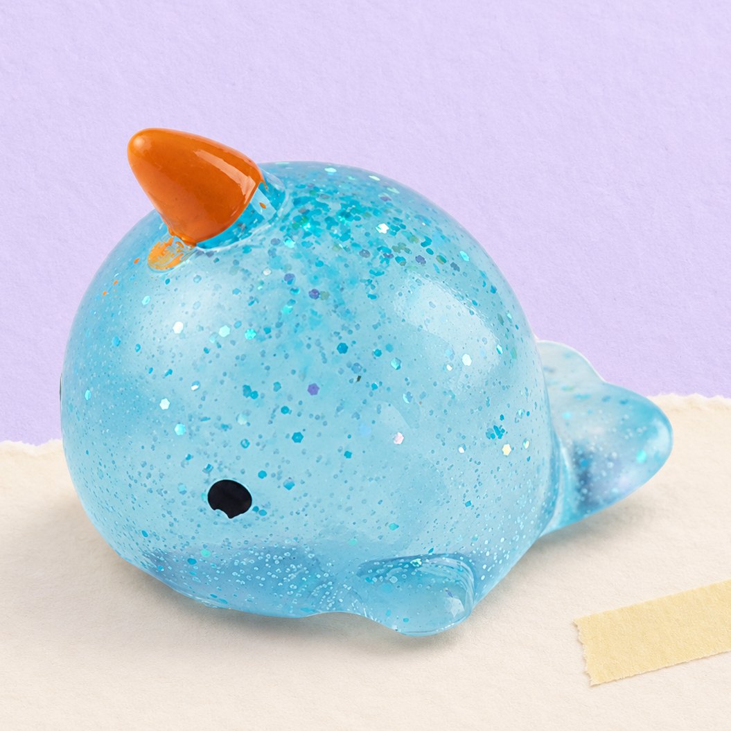 Narhval-squishy med glimmer, produktfoto på pastelfarvet papir