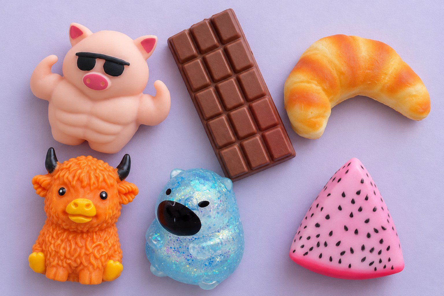 Nové squishy shora na fialovém: svalnaté prase, čokoláda, croissant, skotská kráva, třpytivá kapybara a dračí ovoce