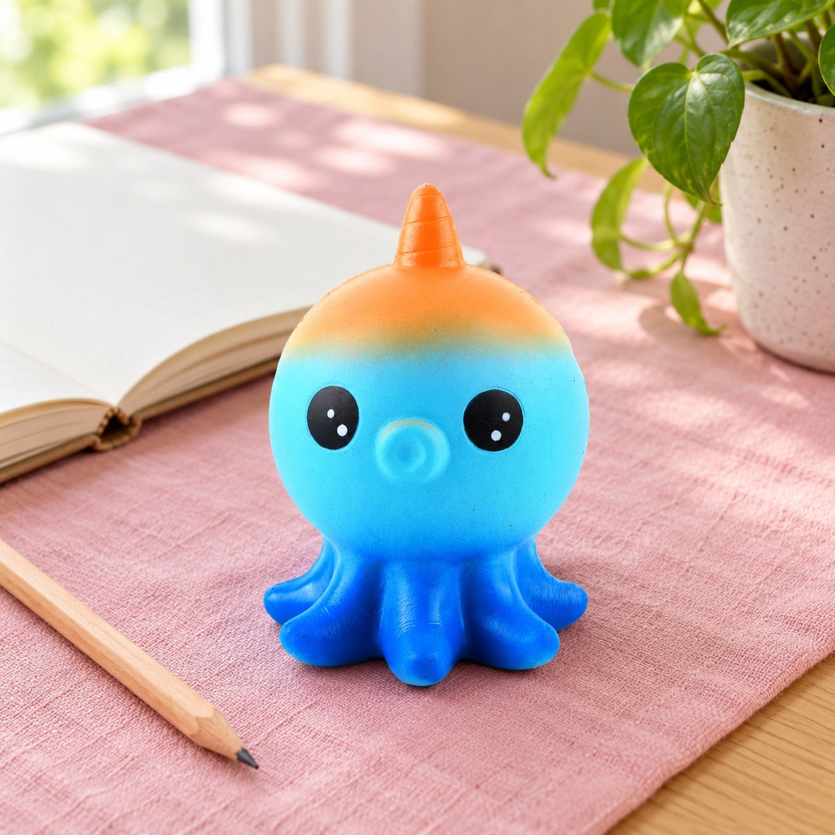 Octopus Squishy, Slow Rising, on a desk with a notebook and pencil