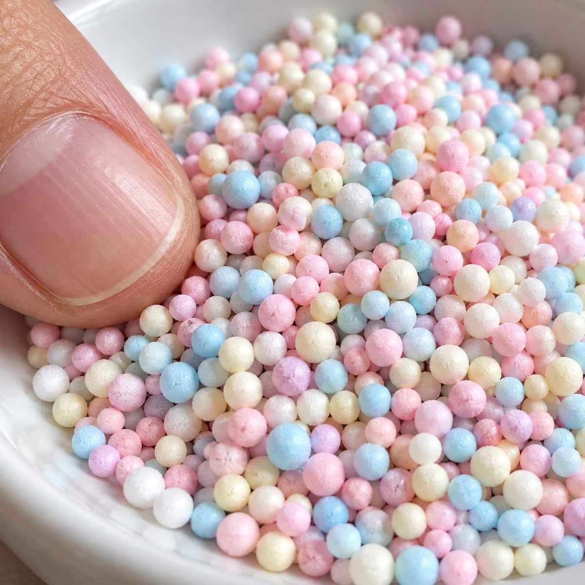 Palline schiuma pastello da vicino, con la punta del dito per le dimensioni
