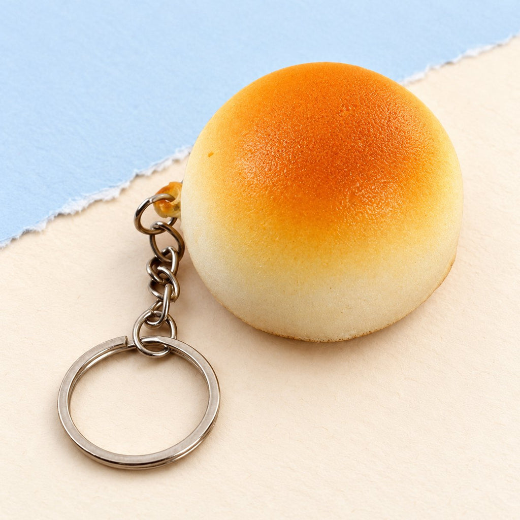 Porte-clés squishy petit pain doré de 4 cm, slow rising, posé sur un papier pastel