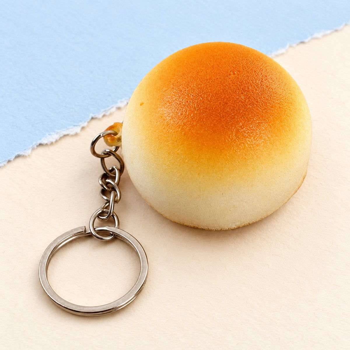Porte-clés squishy petit pain doré de 4 cm, slow rising, posé sur un papier pastel