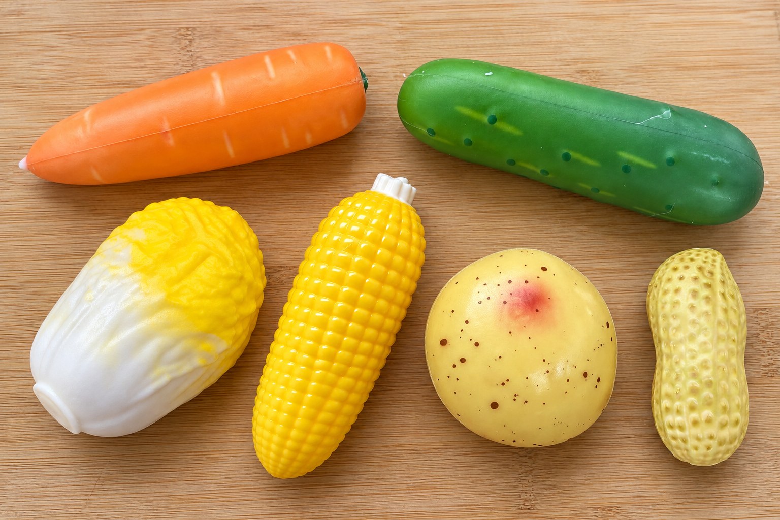 Seis squishies crunchy de verduras en una tabla de madera vistos desde arriba: zanahoria, pepino, col, maíz, patata y cacahuete