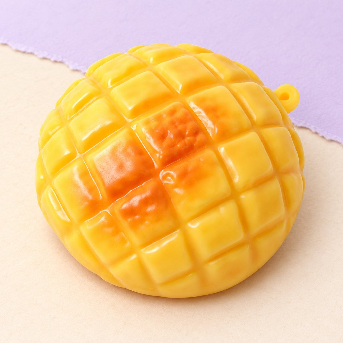 Squishy ananasová bulka o velikosti 9 cm na pastelovém papíře