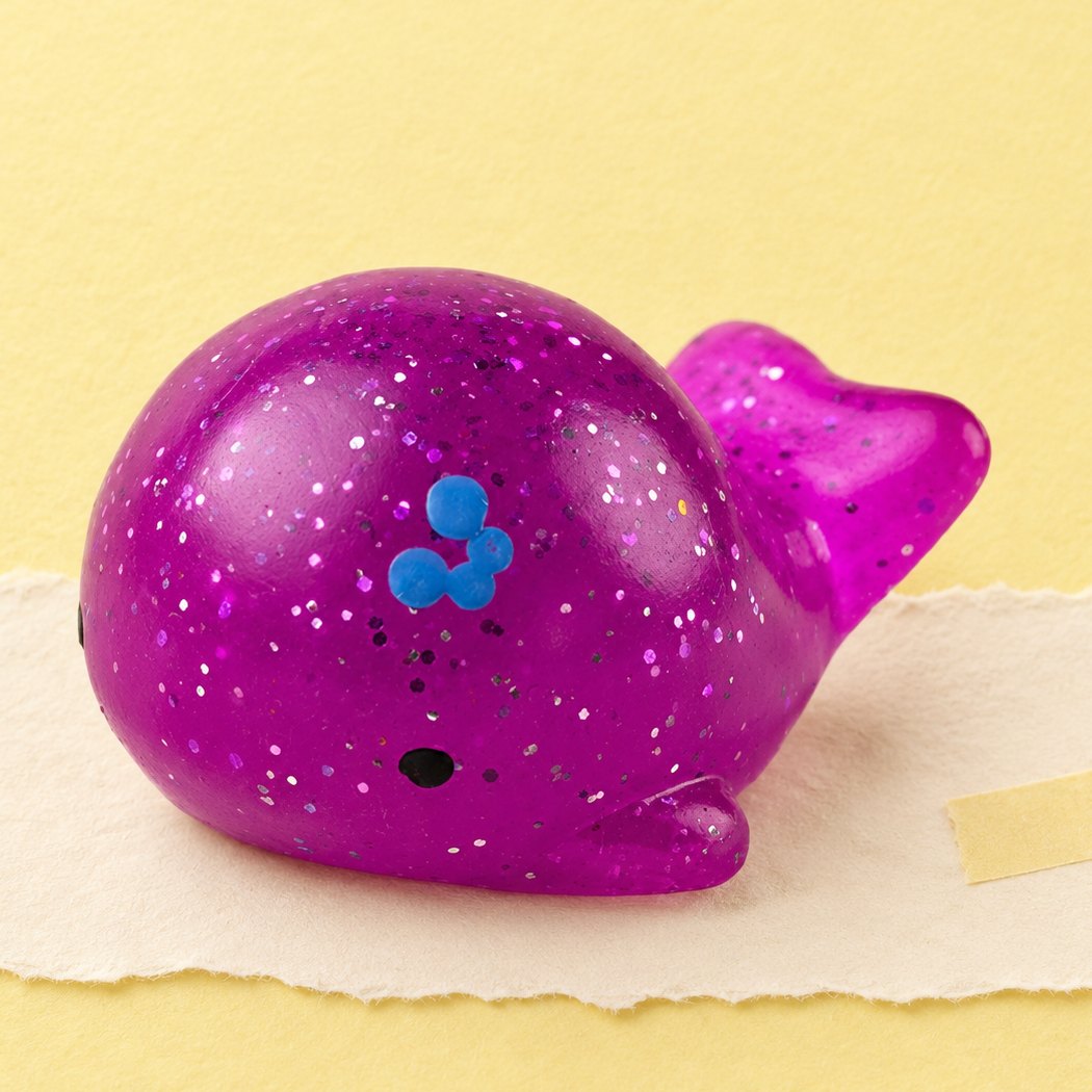 Squishy baleia mochi com brilhantes, sobre papel pastel