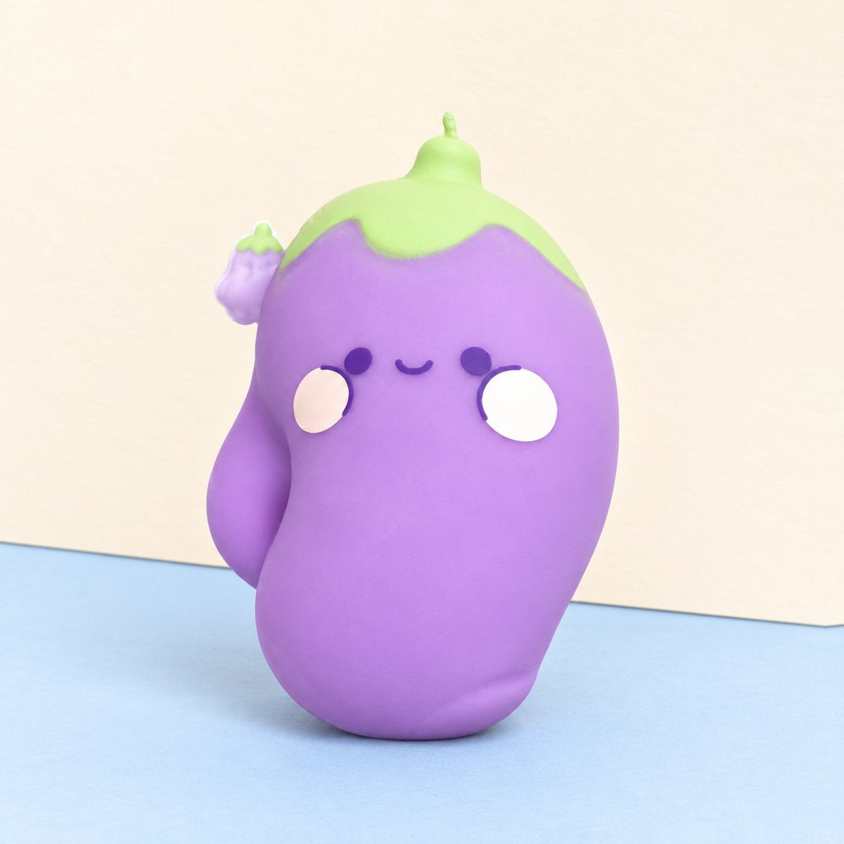 Squishy berenjena con carita kawaii sobre papel pastel