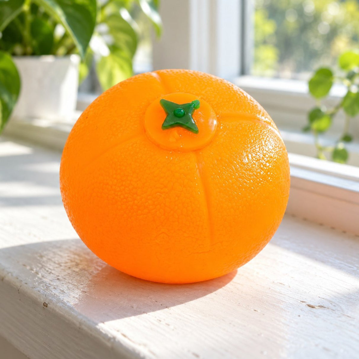 Squishy bola de agua naranja en el alféizar de una ventana soleada