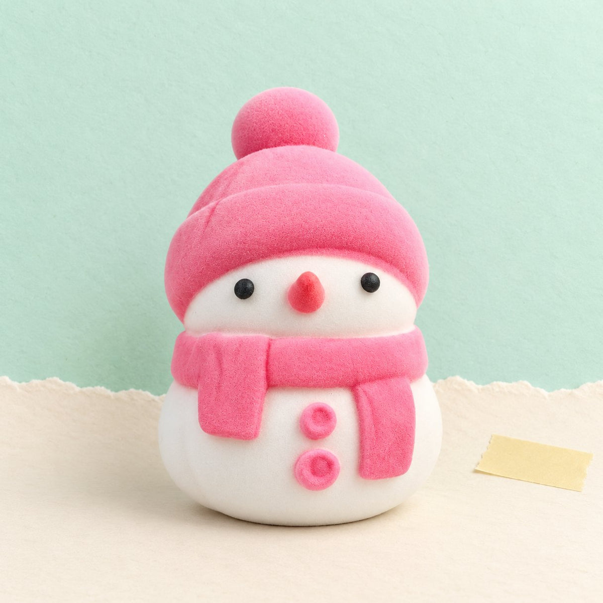 Squishy bonhomme de neige mochi rose dans son sachet, sur papier pastel