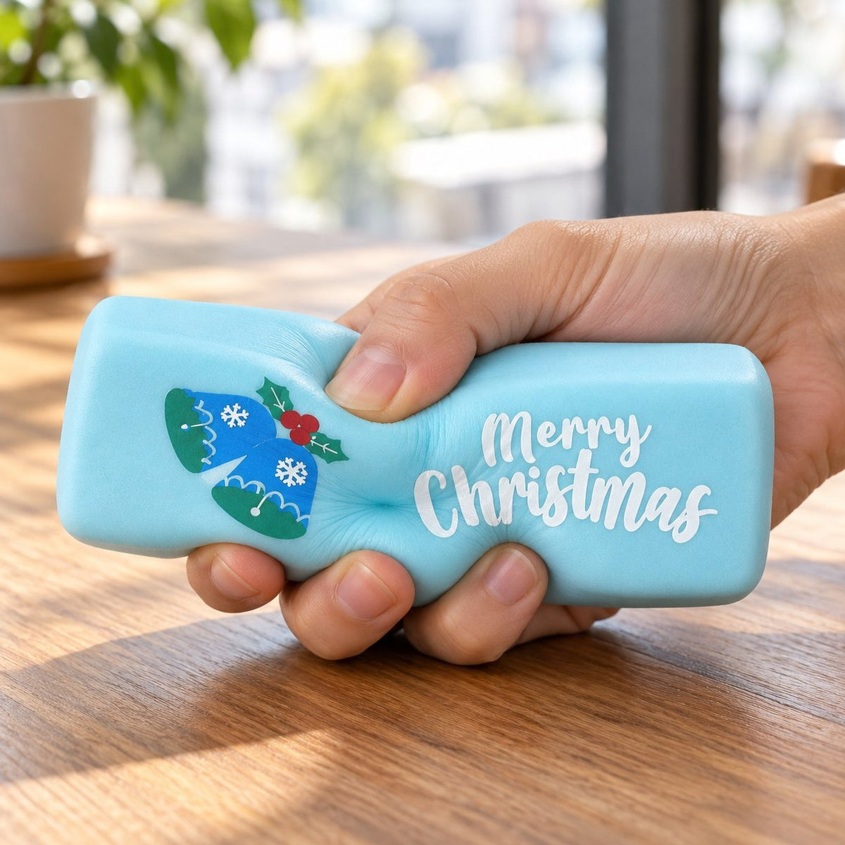 Mano che schiaccia lo squishy burro Merry Christmas azzurro con muffola, tra i 6 colori