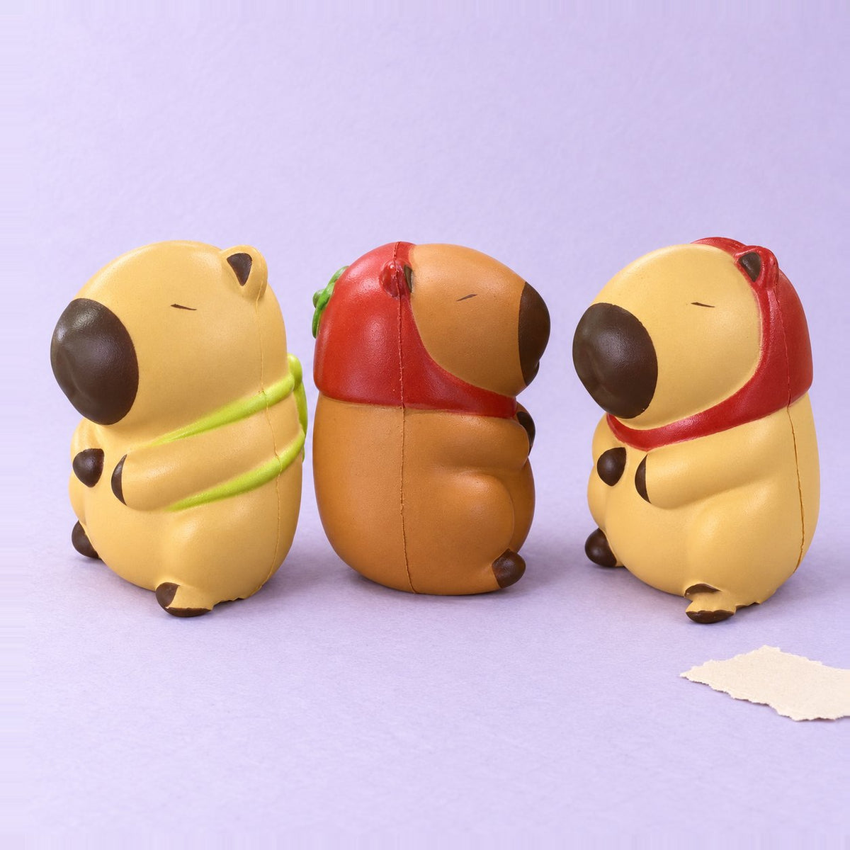 Set de squishy capibara slow rising con los 3 modelos, sobre papel pastel