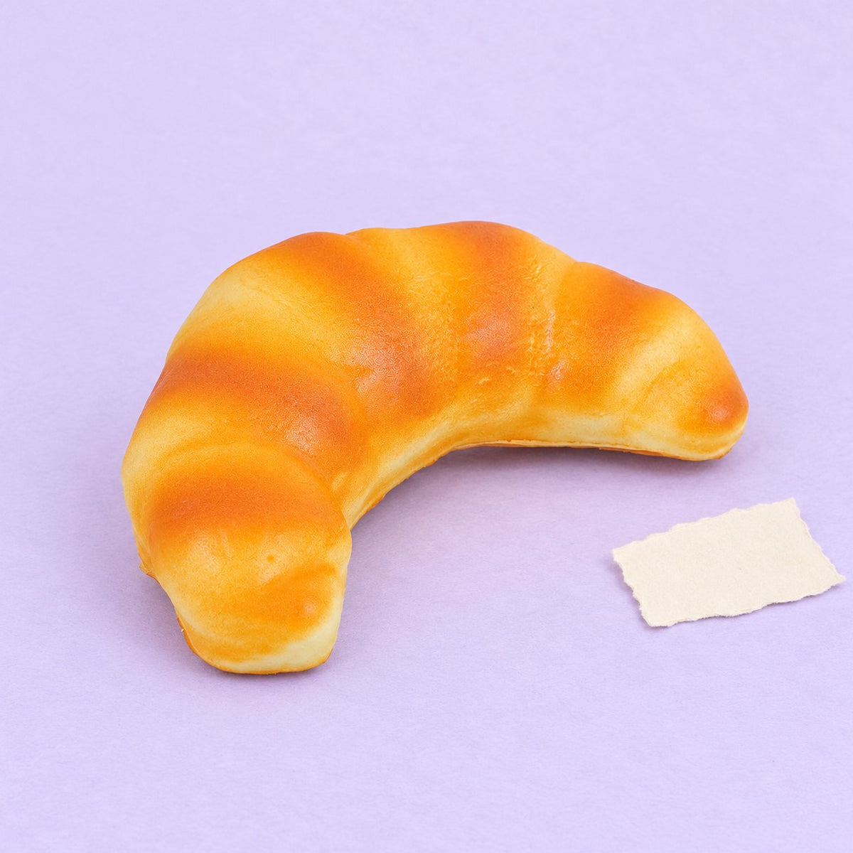Squishy Croissant aus PU, 12,5 cm, Slow Rising, Produktfoto auf Pastellpapier
